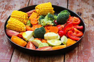 Mixed vegetables in the round baking pan are waiting for the baking on the wooden table, rustic style, super healthy, close-up, top view