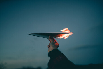 Human hand with burning paper airplane in the sky