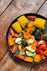 Super tasty oven roasted vegetables in black baking dish are lying on the wooden table, super healthy! Close-up, rustic style, top view