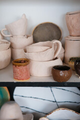 Clay products of different sizes. Colorful kitchen items on the shelf. Handmade plates and cups