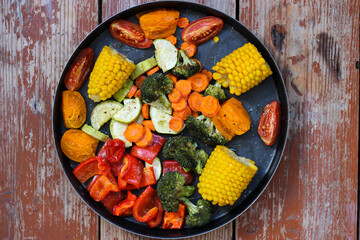 Super tasty oven roasted vegetables in black baking dish are lying on the wooden table, super healthy! Close-up, rustic style, top view