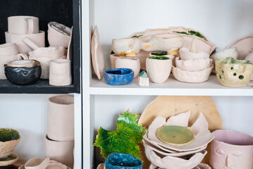 Clay products of different sizes. Colorful kitchen items on the shelf. Handmade plates and cups