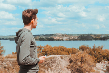 Fototapeta na wymiar A young guy in a sweatshirt holds a phone in his hands and enjoys the view of the quarry and the lake on a warm spring day.