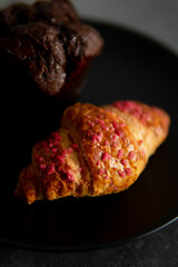 croissant with raspberries and chocolate muffin on a black plate.