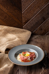 Pasta Carbonara. Spaghetti with bacon, parmesan, cream sauce and egg yolk. Isolated on a grey round plate with silver cutlery and sacking on wooden background. Mediterranean gourmet food. Copy space.