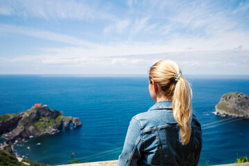 A lonely blonde in a denim jacket looks at the sea and rocks in the Bay of Biscay, Spain. Selective focus. Copy space
