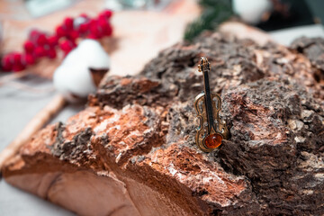 Decoration in the form of a violin of bronze and amber against the background of birch log