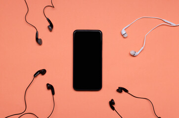 Top view of blank smartphone screen and many earphones on the orange surface.Concept of audio chat...