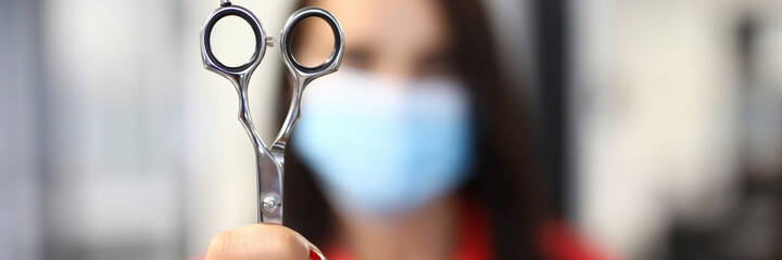 Woman in protective mask hold scissors in hand closeup. Professional work of master with hair. Haircut and hair styling in beauty salon. Training and getting hairdresser profession concept.