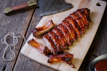 Glazed baby pork ribs BBQ with sesame, sauce and hatchet for meat on wooden background