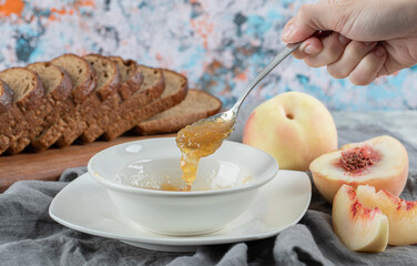 Hand taking a spoon with peach jam in white plate