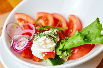 Vegetable salad with tomato, cucumber, bell pepper, onion and sour cream on the white plate. Close-up, selective focus