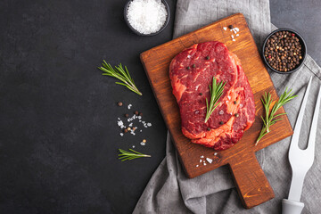 Raw rib eye steak of beef with rosemary on cutting board