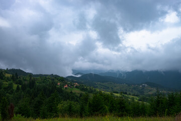 A view of the slopes of the hills covered with trees and villages, with misty mountains and stormy clouds in the background. Shot in Tara national park, Serbia
