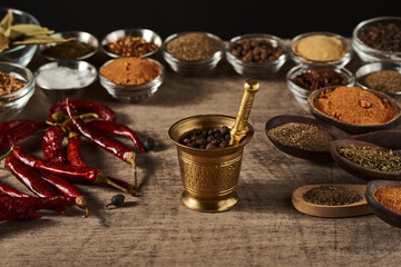 mortar with pepper peas on a background of bowls with spices dried red pepper and wooden spoons with spices on a wooden surface