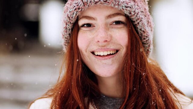 Close up portrait of cute charming face of young woman model with red hair, posing looking at camera, smiling and feeling happy. Winter beautiful street outdoor. Slow motion