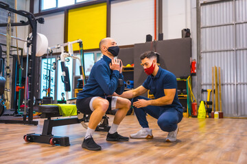 Fototapeta na wymiar Personal trainer in the gym correcting the athlete's squats in the coronavirus pandemic, a new normal. With protective face mask