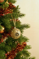 Fototapeta na wymiar A golden ball on the branch of a Christmas tree with decorations. Image with selective focus.