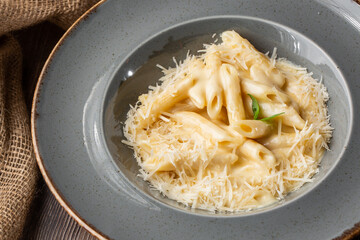 Pasta Penne with parmesan cheese and creamy sauce. Macro close-up of isolated dish in a grey round plate with sacking by side. Mediterranean gourmet food.