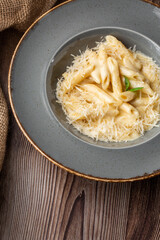 Pasta Penne with parmesan cheese and creamy sauce. Macro close-up of isolated dish in a grey round plate on wooden background with sacking by side. Mediterranean gourmet food.