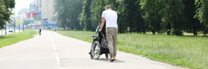 Naklejka premium Nurse ride disabled person in wheelchair. Volunteer service for people with paralyzed limbs. Man walk with woman in wheelchair in the park. Social service for people with physical health problems.
