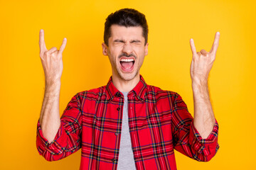 Naklejka premium Photo of sweet funny young man dressed plaid shirt showing rock star sign open mouth isolated yellow color background
