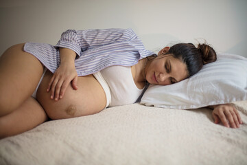 Pregnant woman sleeping on bed and touching her belly.