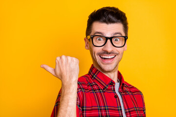 Photo of positive funny guy wear checkered shirt glasses pointing thumb up back empty space...