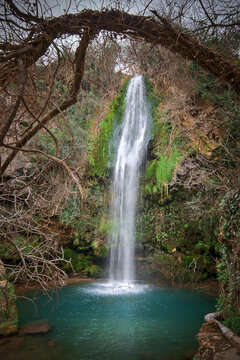 A large beautiful waterfall in a forest with blue water and trees.