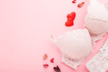 Woman bra, panties and bright red hearts on light pink table background. Pastel color. Closeup. Empty place for romantic text. Top down view.