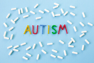 Autism word and a lot of pills and capsules on a blue background. Dietary supplements, nutraceuticals and vitamins for people with autism. World autism awareness day, autism month. Selective focus.