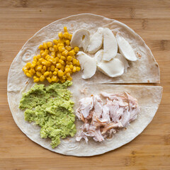 Making tortilla wrap with chicken, avocado, sweet corn and mozzarella cheese.