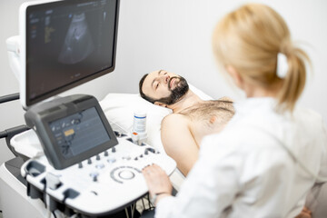 Doctor examining liver of male patient with ultrasound scan in medical clinic. Health and wellness concept.