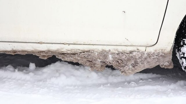 Detail view of frozen salt, snow and ice chunks stuck under car body, causes rust and corrosion in the winter outdoors.