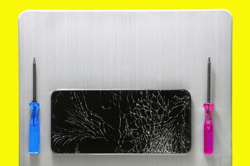 A touch phone with a broken screen and screwdrivers lie on a gray metal brushed surface. Layout with space to copy. A blank for advertising services for the repair of smartphones or gadgets.