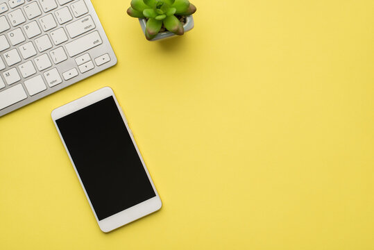 Photo above of plant keyboard and phone isolated on the yellow background
