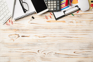 Photo above of notebook calculator phone stapler paperclips glasses and pen on the wood table