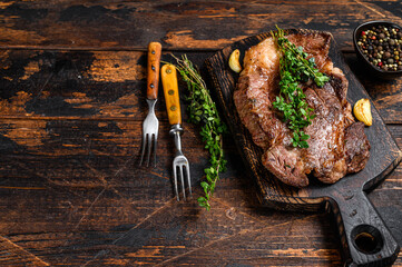 Grilled Chuck eye roll beef meat steak on a cutting board. Dark wooden background. Top view. Copy...