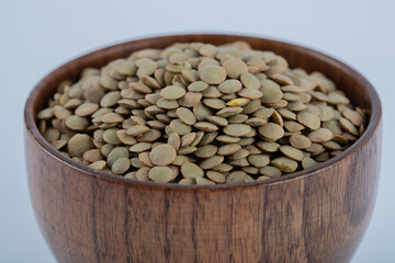 A small wooden bowl full of raw brown lentils
