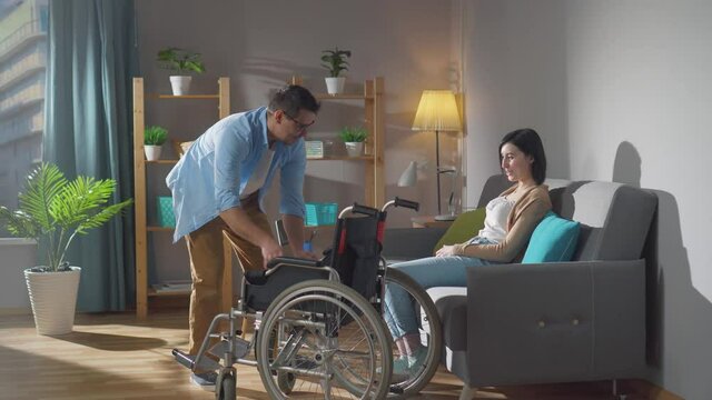 couple of spouses a young disabled woman and her husband help her get into a wheelchair