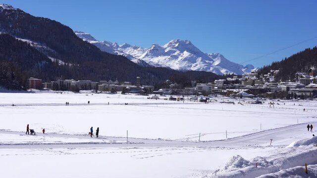 Europe, Switzerland , Saint Moritz February 2021 - Landscape with lake frozen in Sanit Moritz with people walking in the snow during Covid-19 Coronavirus epidemic lockdown - Bernina Express red train 