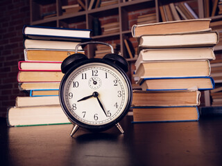 Time for learning concept. Alarm clock and lot of books in the library.