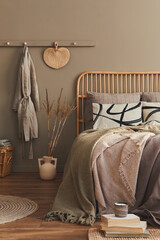 Wooden bed in stylish neutral bedroom interior with design furniture, decoration, carpet, book, dried flowers in vase, bed sheets, blanket, pillows and elegant personal accessories in  home decor.