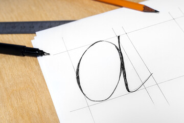 Hand written letter A on white sheet of paper, pencil, ruler and black marker on wooden background....