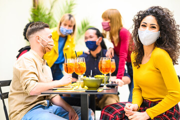 Multiracial people drinking spritz with open face mask at cocktail bar - New normal lifestyle...