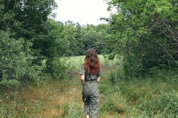 happy brunette woman in overalls on the meadow back view