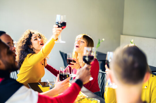 Group of multiracial friends cheering with red wine in trendy winery bar - Happy people drinking and having fun at pub restaurant  - Party and lifestyle concept