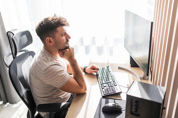 Cheerful young man using computer and smiling while sitting on the sofa. Concept of young business people working at home.