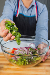 Hands preparing vegetable salad, toss the chopped green onions in a glass bowl.
