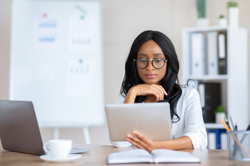 Focused young black business lady using tablet pc at her workplace in modern office, copy space